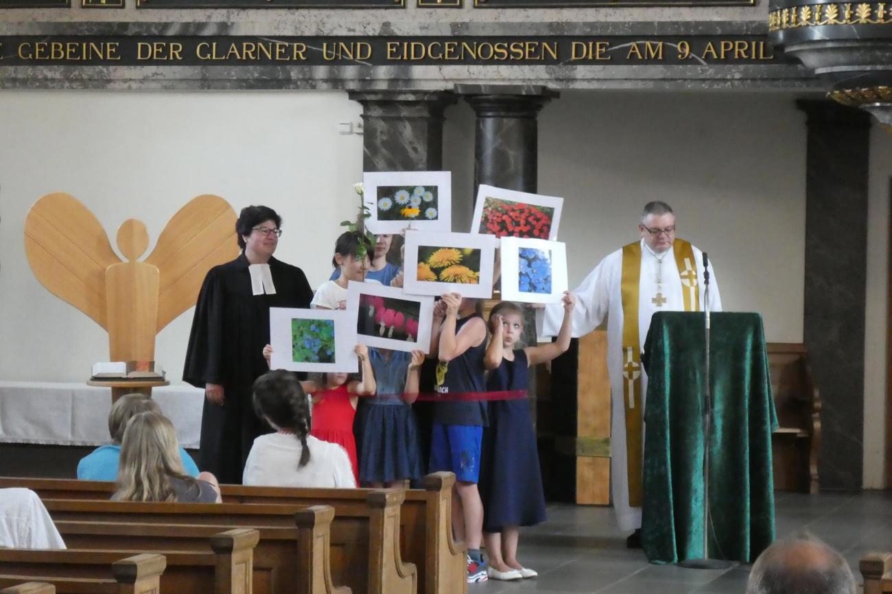 Eine Schulklasse wie ein bunter Blumenstrauss: Szene aus dem ökumenischen Gottesdienst in Mollis mit Pfarrerin Christina Brüll und Dekan Harald Eichhorn.
Bild Johann Beck